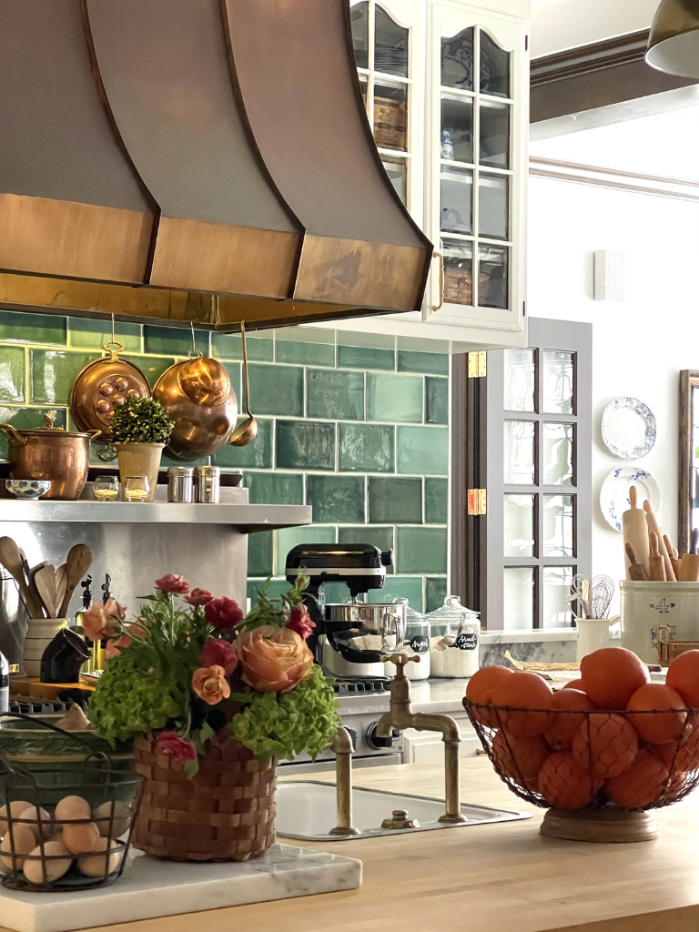 a country kitchen with green tiles from devol, lots of copper and in the style of Nancy Meyers